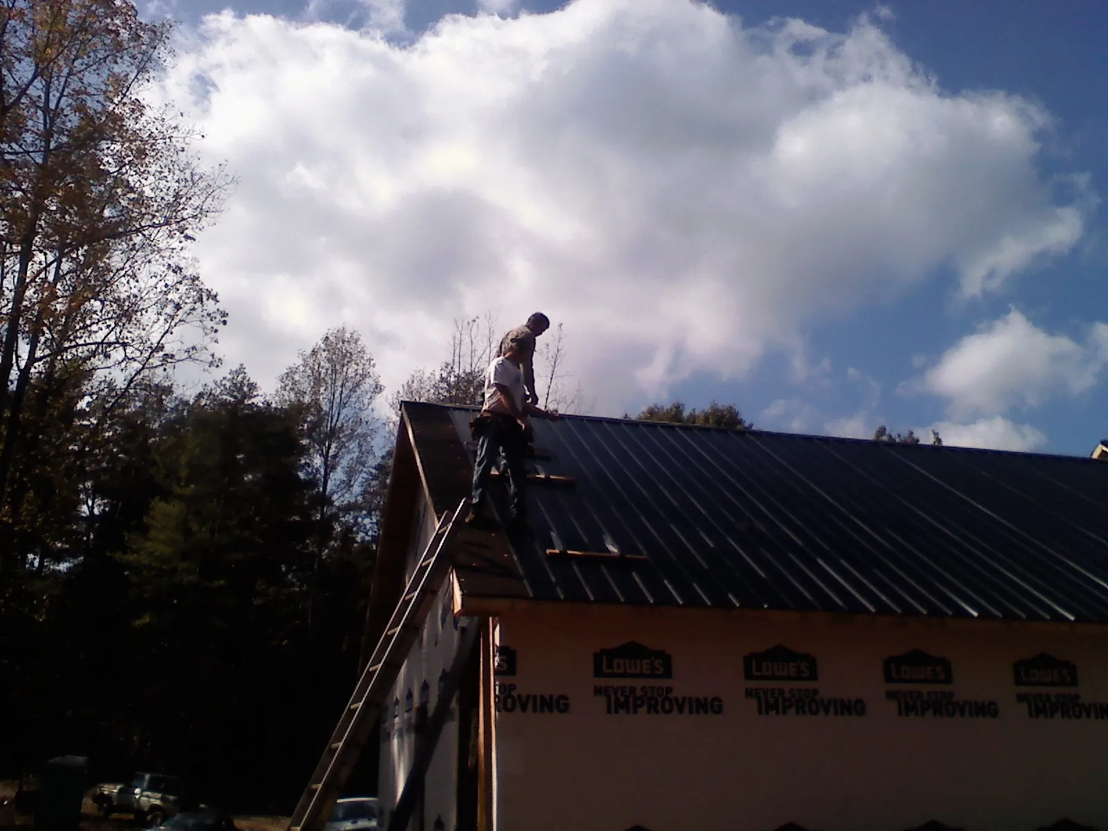 Roofer fastening dark metal panels high against a cloudy sky, from a Roof Inspection job in Buffalo